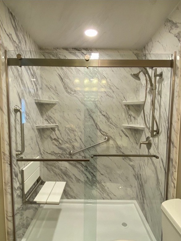 A walk-in shower with a sliding glass door and Venatino marble-look acrylic wall panels